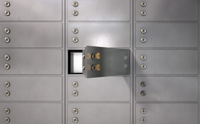 A closeup of a wall of closed metal safety deposit boxes with one open revealing its contents inside