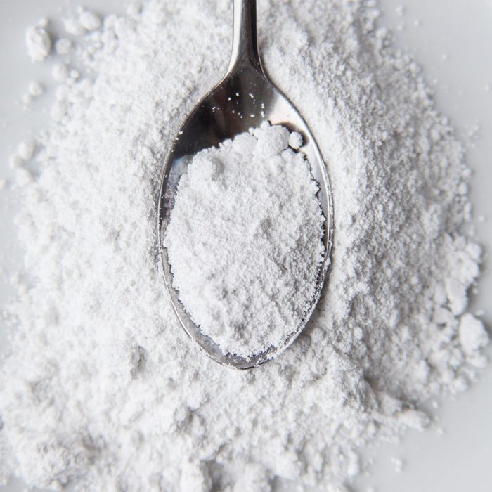 White powder in silver spoon over white background. Top view. Detailed close-up shot. Icing, caster, confectioners or powdere sugar pile