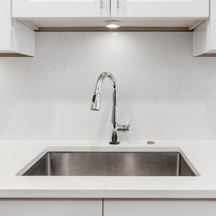 White kitchen built with shaker style cabinets and white granite. Shows stainless dishwasher, granite back splash. Brushed chrome faucet and hardware