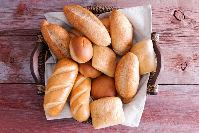 Assorted crusty fresh golden bread rolls in a basket in different specialty shapes displayed on a rustic wooden buffet table as an accompaniment to a meal