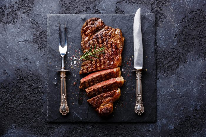Sliced grilled meat barbecue steak Striploin with knife and fork carving set on black stone slate
