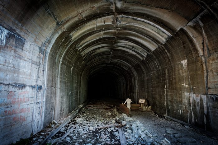 A person stands alone in a very large abandoned train tunnel