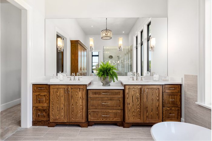 Master Bathroom Interior in New Luxury Home with Dark Hardwood Cabinets, Freestanding Bathtub, and Shower visible in Mirror Reflection