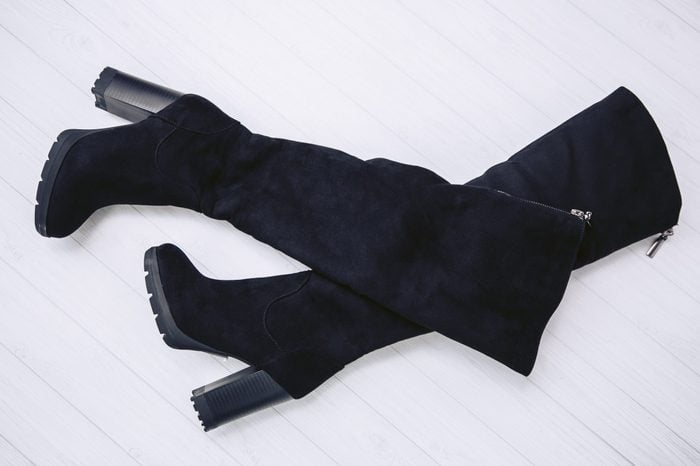 Luxury winter boots with high heels made from genuine black suede leather on a white wooden background