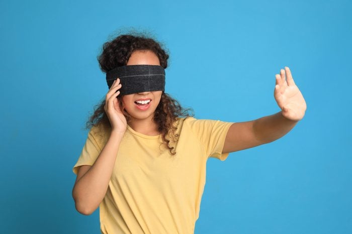 Young African-American woman with black blindfold on blue background