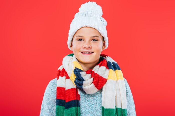 front view of smiling kid in hat and scarf isolated on red