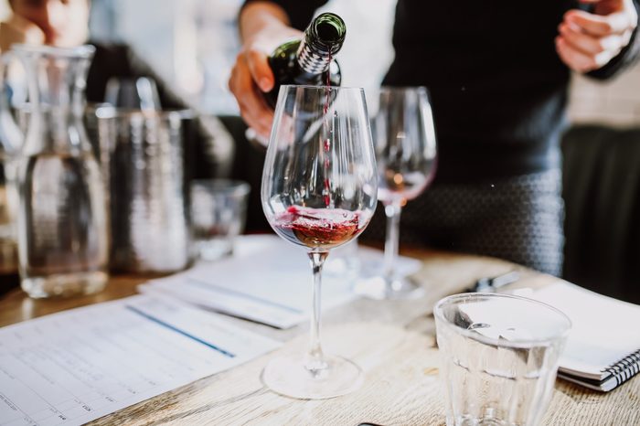 A close up shot of a sommelier pouring red wine into a wine glass. Selective focus point on the wine drops and the glasses. Other glasses in the background are out of focus. Wine training and tasting