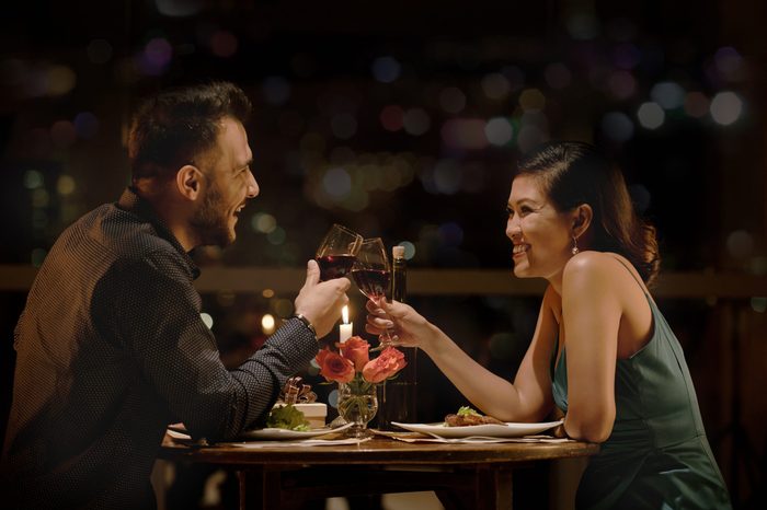 Cheerful couple clinking glasses at late romantic date in restaurant