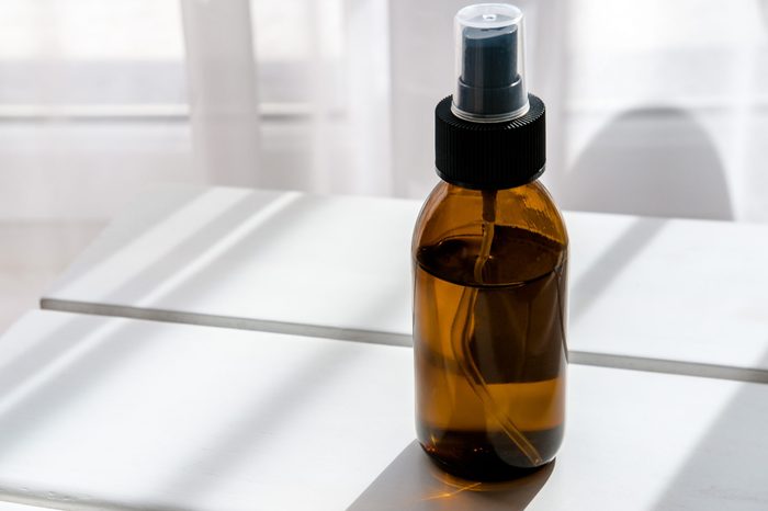 Glass brown spray bottle with organic cosmetics on white table. Direct light. Beauty blogging minimalism concept