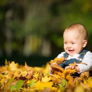 Beautiful happy baby in autumn nature - sitting in leaves