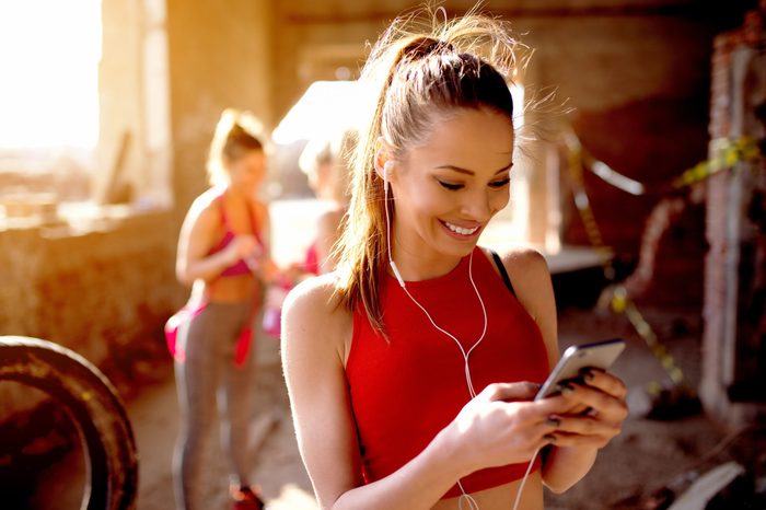 Beautiful young woman listening music fitness training workout. Group of fitness people behind preparing for training.