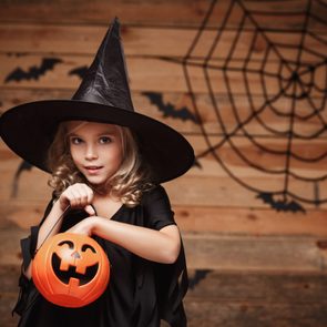Halloween Witch concept - little caucasian witch child enjoy with halloween candy pumpkin jar. over bat and spider web background.