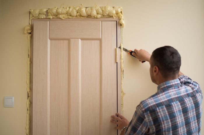 Ð¡utting foam after mounting a door. Handyman knife cuts off excess mounting foam. Installation of doors using polyurethane foam mounting. Polyurethane foam for thermal insulation.