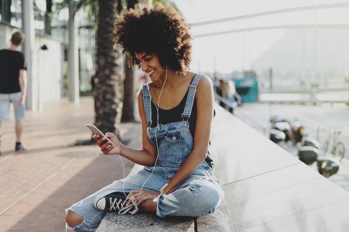 beautiful mixed race girl with afro hair listening to her favorite music through headphones using a mobile phone. an attractive black young woman adds a new track to her playlist using a mobile app