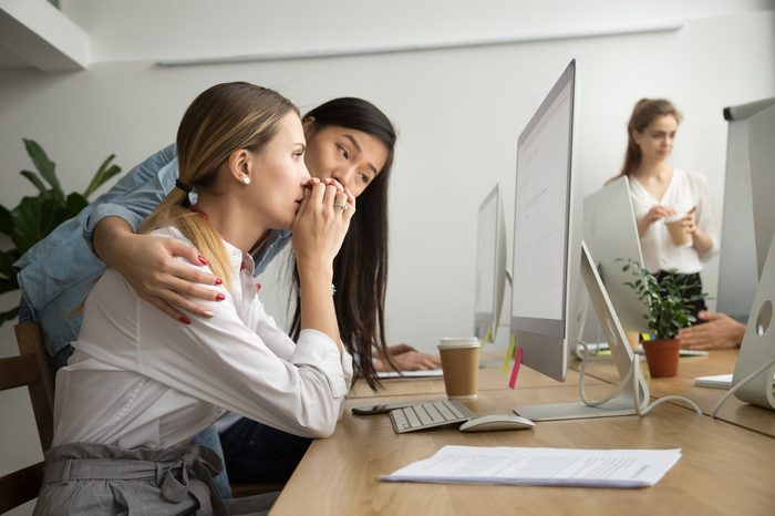Asian colleague embracing supporting caucasian woman reading bad news in email, teammate comforting stressed frustrated female coworker upset by dismissal, helping to solve problem online in office