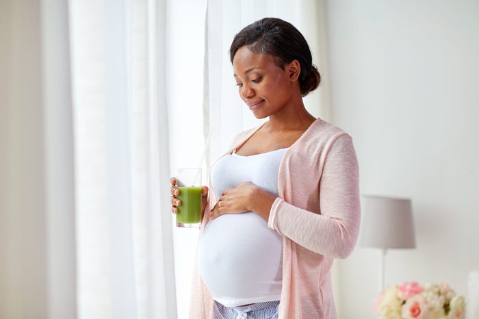 pregnancy, people and rest concept - happy pregnant african american woman drinking green vegetable juice or smoothie at home