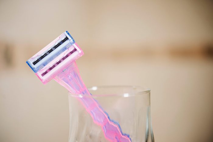 Two plastic blue and pink razors in transparent glass cup in the bathroom