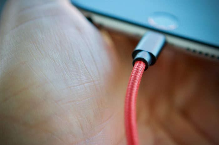 red charging lead plugged into a smartphone held in mans hand
