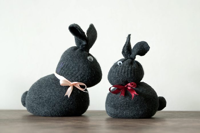 Easter decoration, two cute bunny rabbits, made of textile gray socks with ribbons and eyes. Wooden and light background. Handmade decoration, children joy and activity at home. Easter concept.