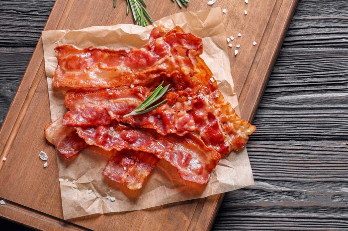 Board with fried bacon on wooden background