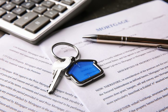 Key with trinket, pen and calculator on mortgage contract