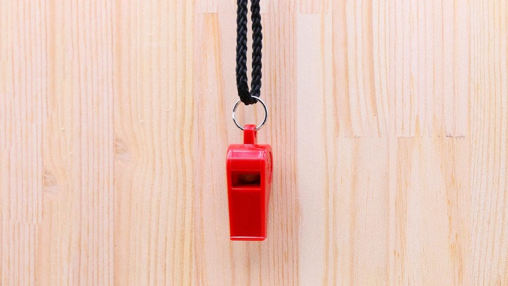 Red plastic Whistle on brown wooden background in sport object concept. Whistleblower concept.