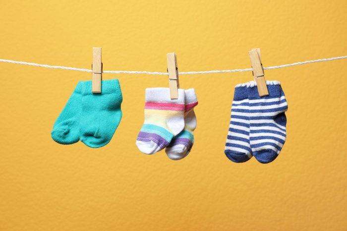 Different socks for baby on laundry line against color background