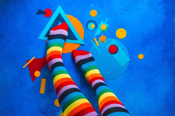 Girl legs in rainbow striped socks on a colorful background with color blocking simple shapes. Abstract geometry flat lay