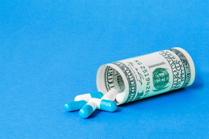 Money dollar rolled up with pills flowing out isolated on blue background, high costs of expensive medication concept. Copy space.