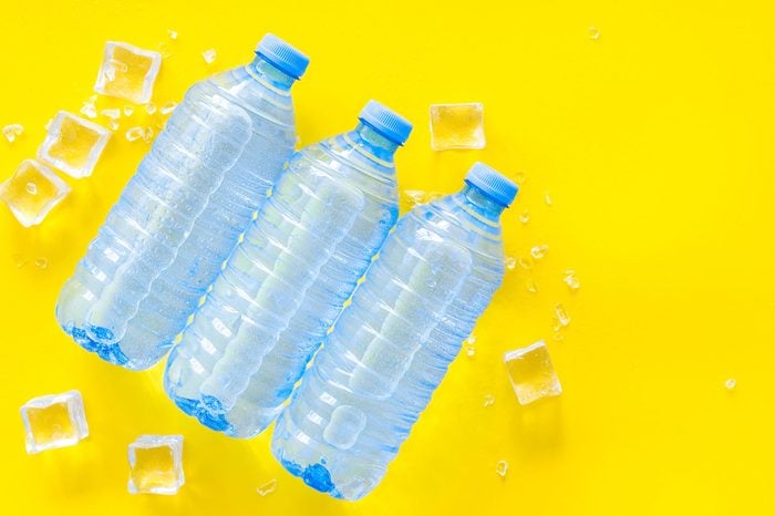 Plastic bottles with pure water and ice on yellow background top view space for text
