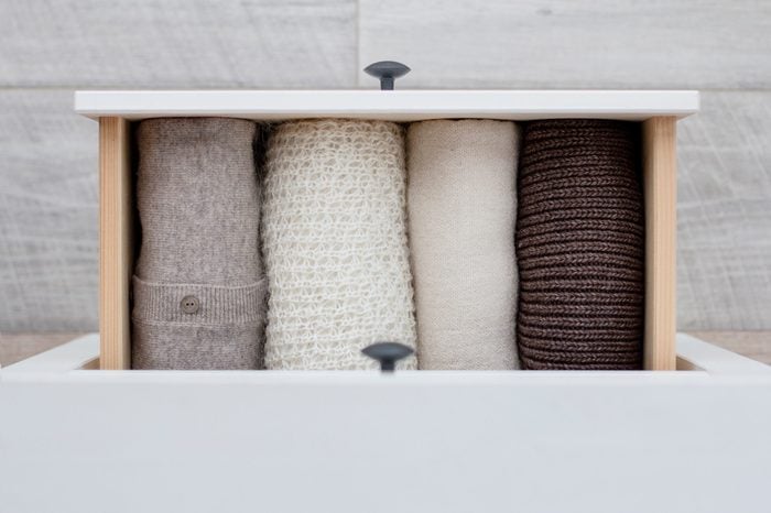 warm knitted women's clothing in brown, white and beige colors in the drawer of the chest of drawers on the background of the wooden floor, top view