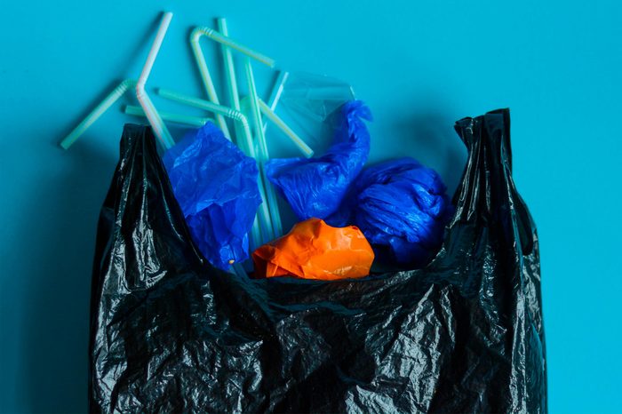 Black plastic bag with variety elements of plastic in it, against a blue background. Representation of plastic pollution