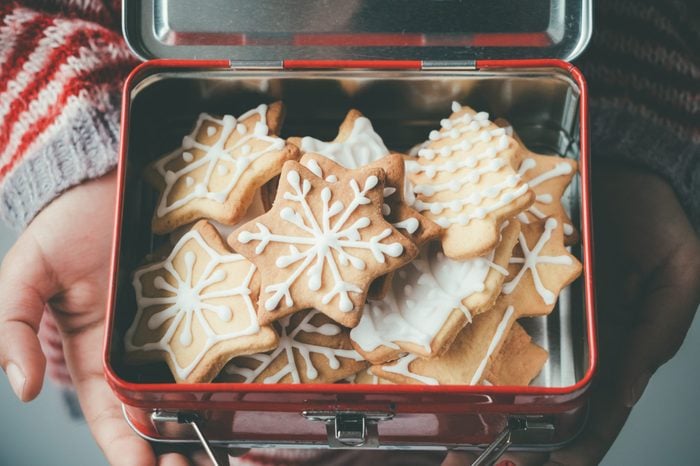 Child hands holding a vintage lunch box full of decorated Christmas cookies