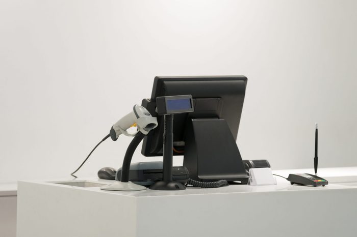 Cash desk with computer screen and barcode scanner on white table and wall in small store