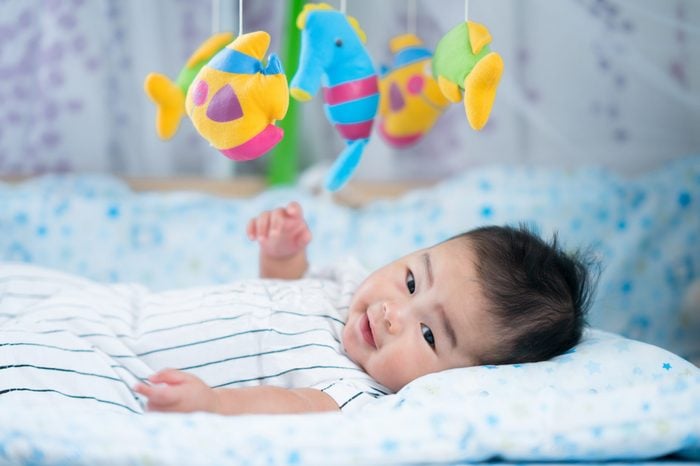 Asian newborn baby smile in a bed with fish and animal mobile. for mom, mother, family concept