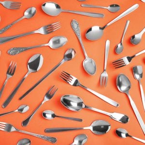 Set of new silver cutlery on coral background, flat lay