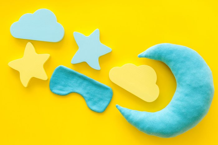 Night sleep concept with moon, clouds, stars toys and blindfold on yellow background top view