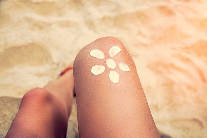 Legs of a girl lying on a beach deckchair by the sea. The sun, painted on sunburnt skin of the foot with sunscreen. Toning