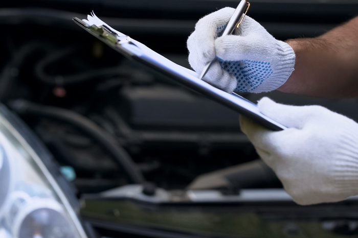 Mechanic diagnoses car, writing costings, annual vehicle inspection, close up