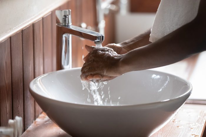 Crop close up of african American man clean hands in pure water from tap or faucet, perform morning cleanup routine at home, biracial male wash in modern design sink after having shower in bathroom