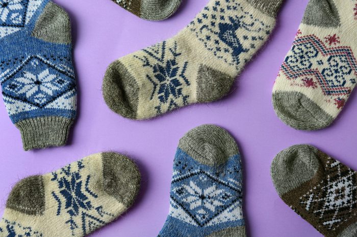 Different knitted socks on violet background, flat lay. Winter clothes
