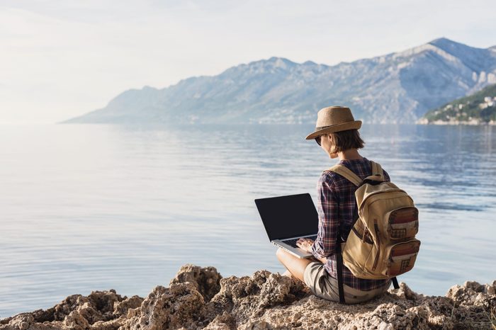 Young woman using laptop computer on a sea. Freelance work concept.People using devices to plan trips, check in to hotels and flights, stay connected to family and office from remote part of the world