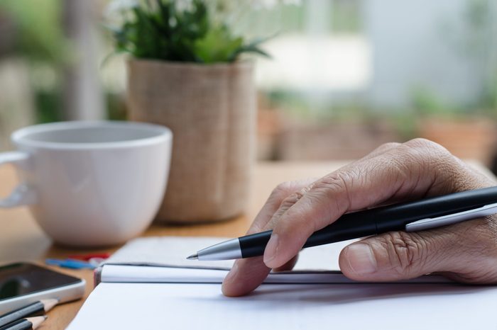 Man's hand holding a pen on paper notebook on table in relax position.