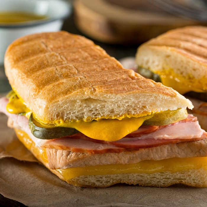 An authentic cuban sandwich on pressed medianoche bread with pork, ham, cheese, pickle, and mustard
