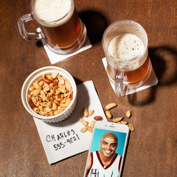 still life on wood. two mugs of beer, peanuts, cocktail napkin, phone showing charles barkley in a basketball uniform