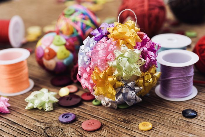 closeup of some handmade christmas balls, mad with ribbon bow, strings and buttons of different colors, and a pile of different haberdashery items on a rustic wooden surface