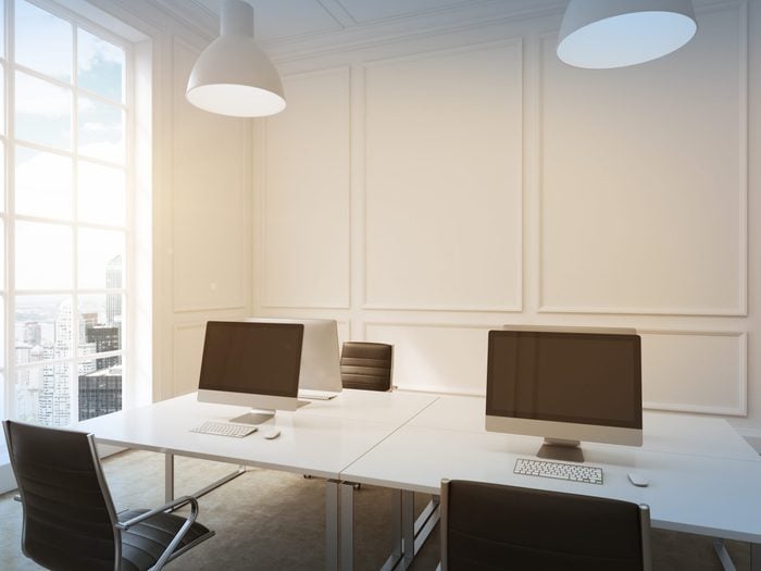 Four workplaces arranged in pairs symmetrically with computers only on them. Four leather chairs around the table. Window with city view to the left. Filter. 3D rendering.