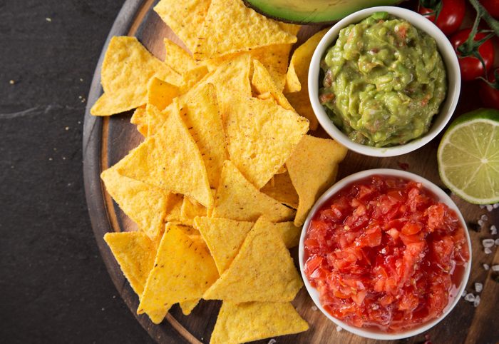 Green Guacamole with nachos and avocado on stone background