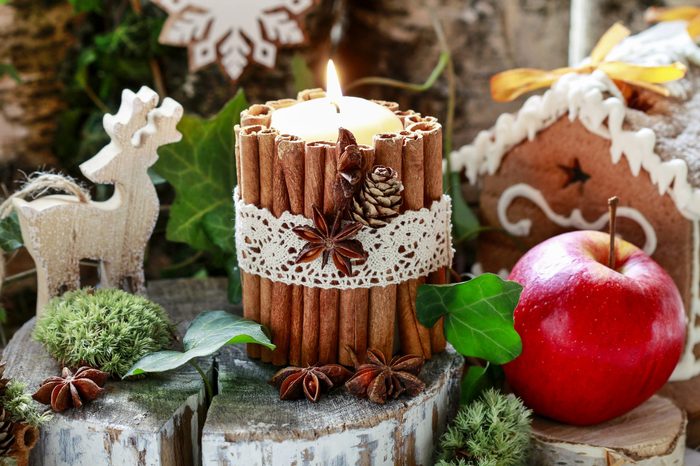 Candle decorated with cinnamon sticks, moss, ivy leaves and wooden deers - beautiful natural Christmas arrangement. 