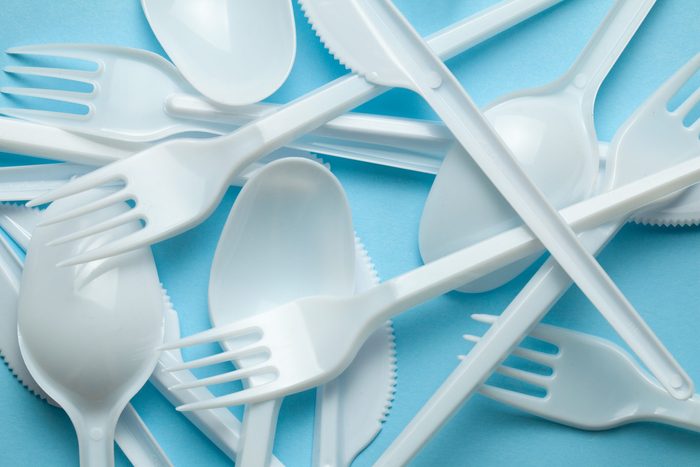 Plastic cutlery, forks, spoons and knives. Pollution of the environment with plastic and microplastics. Blue background.